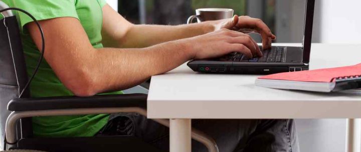 A man in a wheelchair is working on his laptop 